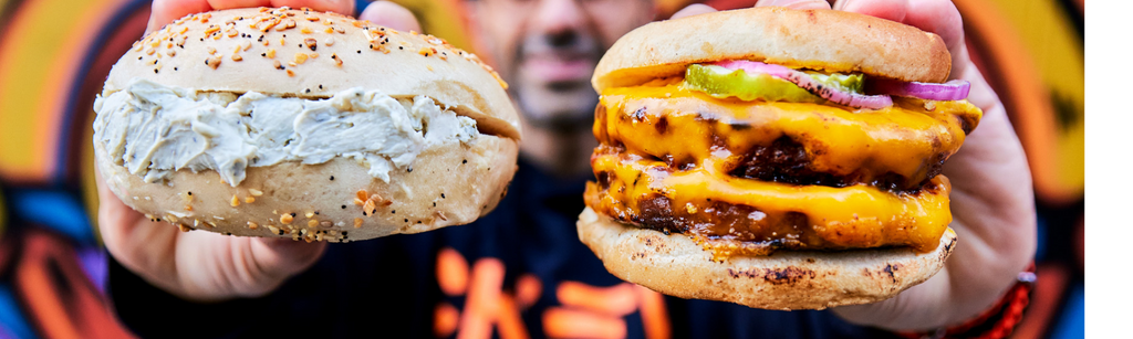 Picture of a man holding a bagel with cream cheese in one hand and a double burger with melted cheddar on each burger in the other